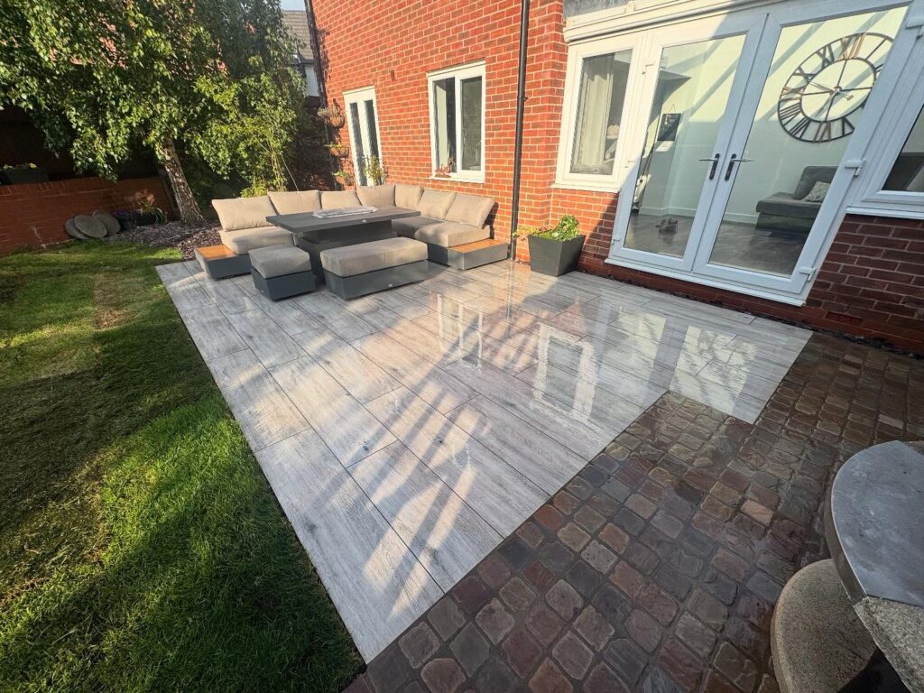 patio layed using decking wood paving slaps with corner sofa on it .